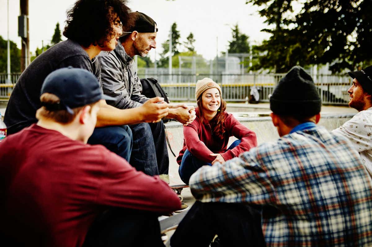 Group of young skateboarders sitting in discussion with mature skateboarder in neighborhood skate park